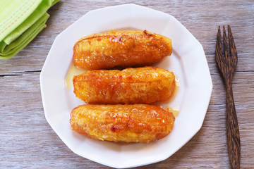 Top view of baked bananas with honey on a white plate on a wooden table.