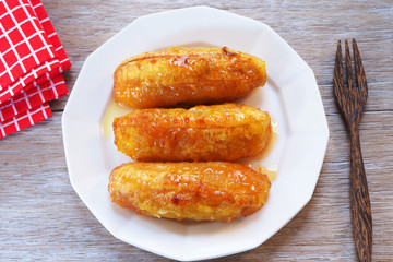 Top view of baked bananas with honey on a white plate on a wooden table.
