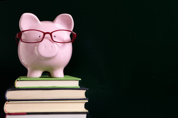 Piggybank or piggybank wearing glasses in front of a school or college blackboard education saving...