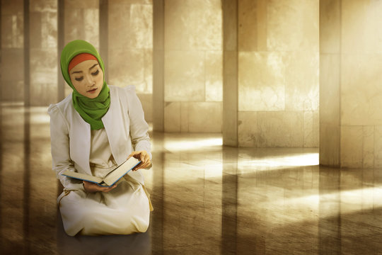Young woman asian muslim wearing hijab, reading the koran