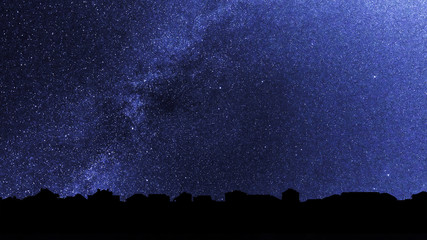 Starry sky over the roofs of suburban houses. Background with millions of stars over the village. Dark skyline in the backlighting. - obrazy, fototapety, plakaty