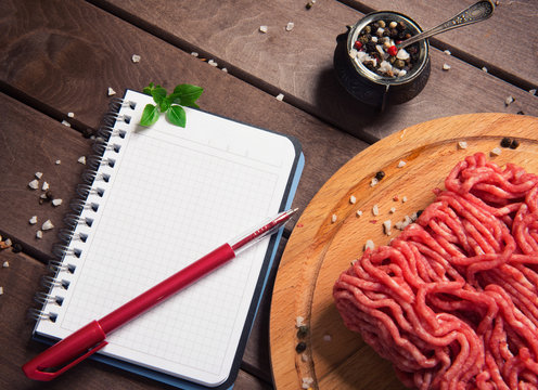 raw minced meat and blank notepad on rustic wooden background