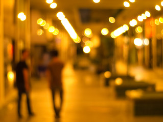 blurred image of two people walking in an alley with many light posts being turned on at night