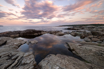 Landscape of a pond in shape of the star surrounded by cracked granite rocks. Standing water reflect clouds glowing by warm light of summer sunset. Russian north, Karelia, Ladoga