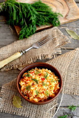 Risotto with vegetables in a clay bowl, fork, dill sprigs, cutting board on old wooden background. Rice cooked with tomatoes, carrots, garlic and spices. Simple and healthy vegetarian rice dish