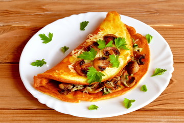 Stuffed omelette on a plate and on a wooden table. Omelette stuffed with grated cheese and fried mushrooms and served with leaves of fresh parsley. Simple and delicious egg dish
