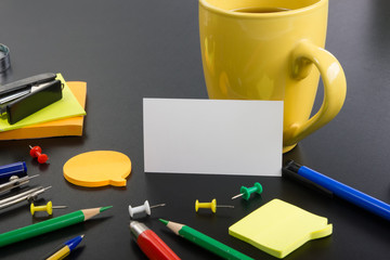 White blank business card. Office table desk with set of colorful supplies, cup, pen, pencils, flower, notes, cards on black board desk table background. Top view and copy space for ad text