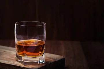 Papier Peint photo Alcool Glass of scotch whiskey and ice on a wooden background with copyspace
