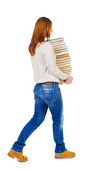 Girl comes with  stack of books. side view. Rear view people collection.  backside view of person.  Isolated over white background. The girl in a white warm jacket bears a huge stack of books