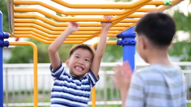 Two young asian boy hang the yellow bar by his hand to exercise at out door playground