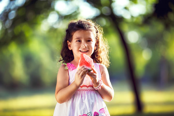 Funny kid eating watermelon outdoors in summer park, focus on eyes. Child, baby, healthy food. Youth lifestyle. Happiness, joy, holiday, beach, summer concept.

