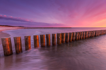 Colorful sunset on Batlic sea beach with wooden groyne