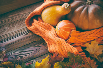 halloween pumpkins shrouded  in cozy knitting orange sweater, fallen leaves on wooden table