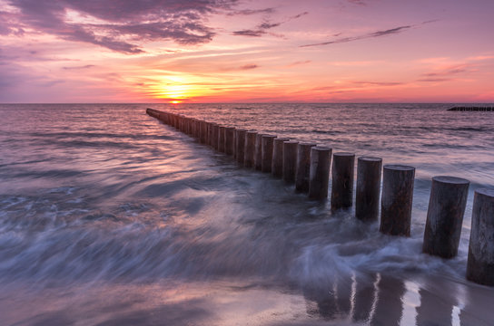 Colorful sunset on Batlic sea beach with wooden groyne