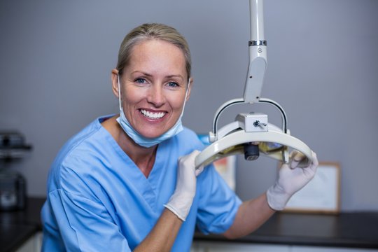 Smiling dental assistant adjusting light in clinic - Powered by Adobe