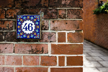 Hand-painted decorative house number tile on a brick wall – 46 (forty-six)