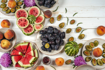 Colorful fruit set of purple, red and orange background in bowls. Plum, peaches, watermelon sliced above white tabletop