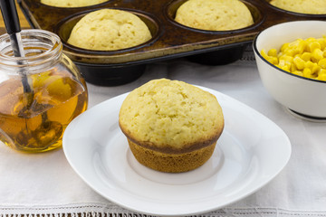 Corn muffin in plate with muffins in pan, syrup and corn in a bo