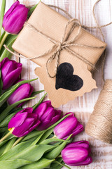 Gift box and tulips bouquet on white wooden background - retro style
