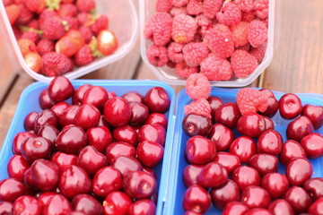Juicy ripe cherries in blue boxes and  strawberries, raspberries in background