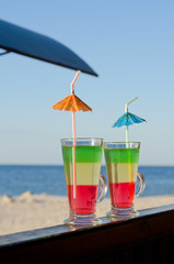 Two colorful cocktails with straws on the background of the beach