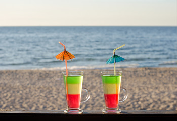 Tricolor cocktail on the bar counter with a sandy beach overlooking the sea, relax