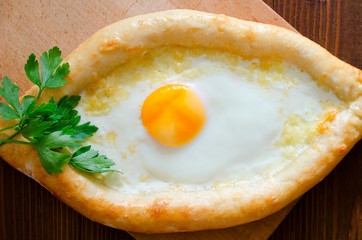 Fresh Ajarian khachapuri with egg and cheese on a wooden board,  Georgian cuisine