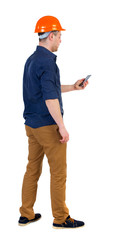 Backview of business man in construction helmet stands and enjoys tablet or using a mobile phone. Standing young guy. Rear view people collection.  backside view of person.  Isolated over white