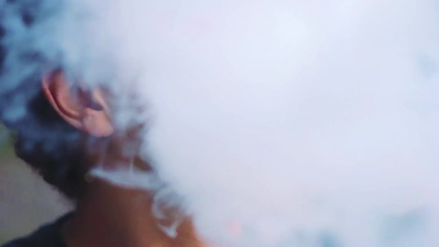 young vaper man exhaling big clouds of smoke with e-cigarette vape in slowmotion