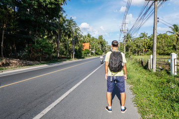 Male tourist stands on roadside by highway in Asia