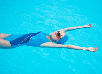 Woman is relaxing in a pool in the blue swimsuit and sunglasses.