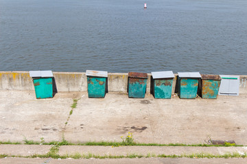 Six (6) green garbage containers standing on the stone embankmen