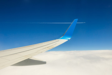 Obraz premium Wing of an airplane flying above the clouds on blue sky background