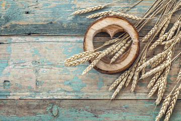 Background with ears of wheat and wooden hearts on old blue boar