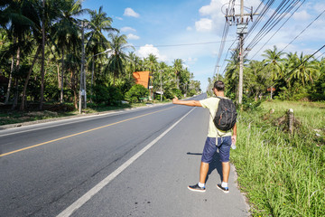 Male tourist hitchhiking on roadside by highway on Samui island, Thailand