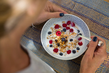 Over shoulder view of woman eating cereal and berry breakfast