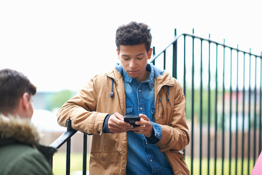 Young male college student reading smartphone text on campus