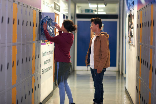 Young female student removing jacket from college locker