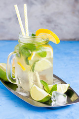 Summer drink, lemonade, mojito cocktail with mint, lemon, lime and ice on blue background