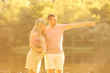 Pregnant couple in the rays of sunlight at sunset. Husband hugs