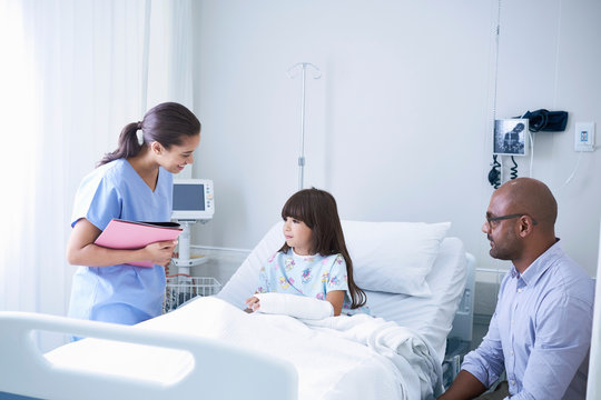 Female Nurse Explaining To Girl Patient With Arm Plaster Cast In Hospital Children's Ward With Father