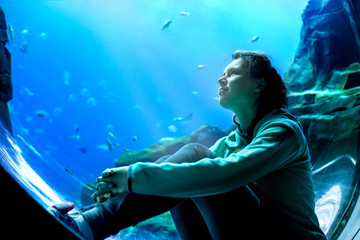 Fototapeta na wymiar Young pretty woman watching fishes in a tropical aquarium