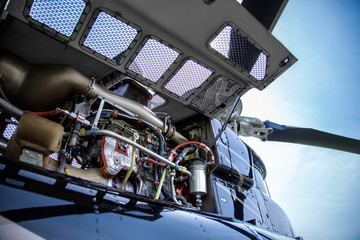 Close up of motor of black with gray stripes bell 407 helicopter standing on green grass field on blue sky background.