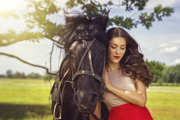 Fototapeta premium Portrait of a young woman with shut eyes standing near a black horse in the park. Focus on a person