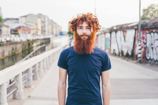 Close up portrait of young male hipster with red hair and beard standing on bridge