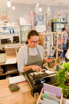 Female sales assistant using till at checkout in gift shop