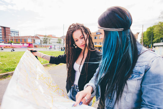 Two young women with dreadlocks and dyed hair pointing at map in urban park
