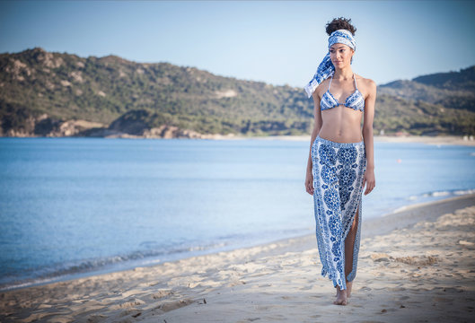Beautiful young woman wearing bikini top and sarong strolling on beach, Costa Rei, Sardinia, Italy