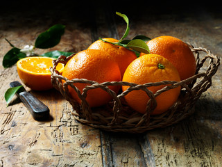 Oranges in basket with one halved in background, rustic wooden table