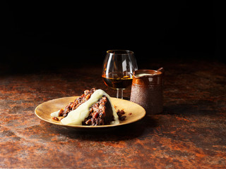 Vanilla and armagnac sauce poured over christmas pudding, glass of brandy and pot of sauce